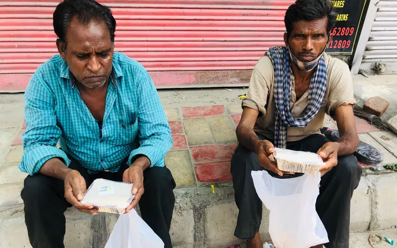 Two workers seated outside a shop holding packed meals